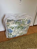 Duvet cover stored inside a clear zippered plastic bag with handle, showing floral pattern through bag.