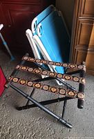 Side view of folding luggage rack with black wood frame and decorative fabric straps with heart and floral motifs.