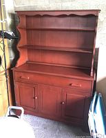 Front angle showing upper shelves with scalloped trim, two drawers and three cabinet doors below, reddish-brown wood finish.