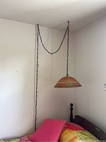 Full view of vintage hanging lamp mounted and suspended by a black metal chain in a corner above a bed with pink and yellow bedding.
