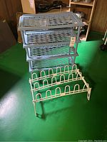 Plastic shelving unit with three removable tiers and white metal shoe holder rack on green cement floor in wooden paneled room.