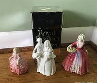 Three Royal Doulton porcelain figurines shown together with the original Royal Doulton box behind them.