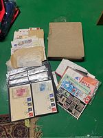 Overview of lot showing large stamp album, envelopes with loose stamps, and multiple plastic sleeves containing stamps and first day covers