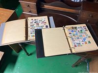 Two open binders filled with pages of vintage stamps on a wooden table.