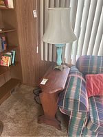 Side view of vintage wood side table with table lamp on top next to couch and wall