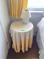 Round pressboard table covered with floral and yellow fabric cover, positioned next to window with yellow curtains