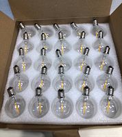 Open box showing 25 clear round LED light bulbs with E12 bases arranged in white foam tray.
