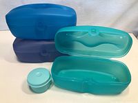 Three plastic Tupperware containers: two large oval shapes in teal and blue with locking lids, and one small round teal container with lid.
