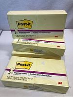 Photo showing four unopened packs of Post-it Super Sticky dispenser notes, yellow color, each measuring 1.5 in x 3 in.