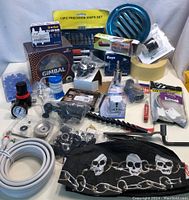 Lot of assorted industrial and mechanical parts arranged on white surface, including precision knife set, various bearings, blue valve, and black fabric cap with skull design.