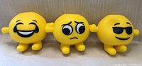 Photo showing three yellow emoji stress balls with different facial expressions: laughing tears, worried eyes, and sunglasses.