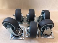 Photo showing six new 1.5-inch castor wheels with metal mounting plates, arranged in two rows of three on a beige surface.