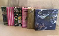 Six packs of napkins in original packaging with various floral and patterned designs displayed side by side.