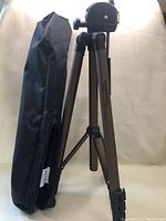 Photo of the camera tripod standing upright beside its black carrying bag on a beige background.