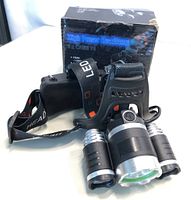 Overall view of the high power headlamp with three LED lights and adjustable strap with the box in the background.
