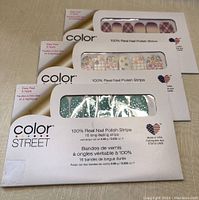 Three packages of Color Street 100% Real Nail Polish Strips stacked, showing the various designs through the window in the packaging.