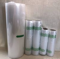 Photo of five rolls of various size vacuum sealer bags, transparent with a textured pattern and green printed markings on some rolls.