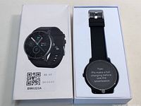 Smart watch in open retail box with black silicone band and protective screen cover showing charging instruction.