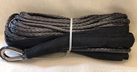 Coiled black synthetic winch rope with metal thimble loop and protective sleeve, secured with white band.