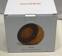 Front of original box showing the Housbay Glows White Noise Machine with wood grain finish and control panel.