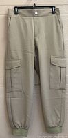 Full view of tan Zara women's cargo pants hanging on black hanger against wood panel wall, showing front button, zipper and cargo pockets.