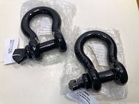 Two black heavy duty D-rings laid on white surface with bubble wrap and tags, showing their new condition and screw pin locking mechanism.