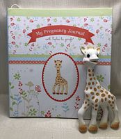 Pregnancy journal featuring Sophie the Giraffe with colorful floral and giraffe-themed cover and an image of Sophie the Giraffe in the center, showing a small mark across the front cover.