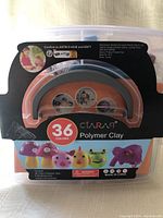 Front label of the plastic storage tub showing branding CLARA9, '36 colors Polymer Clay', with images of small crafted objects and warning label.