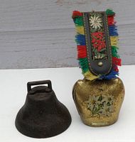 Photo of two vintage bells, one brass with floral design and fringed strap, one small cast iron bell.