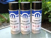 Three Mopar 300g non-chlorinated silicone spray cans with black spray caps outdoors on a wooden surface.