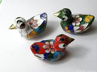Photo showing three small cloisonne ducks in red, green, and white with colorful floral patterns and gold accents.