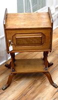 Front view of antique wooden smoking cabinet stand humidor, showing wood grain, front door with knob, and base with shelf and carved legs ending in brass claw feet.