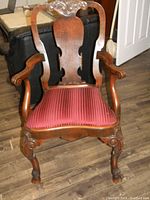 Front view of mahogany arm chair showing carved crest rail, carved arms, and upholstered red striped seat.