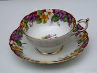 Cup and saucer set showing colorful floral designs on white porcelain with gold rims and highlights.