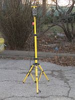 Full view of yellow tripod stand outside on pavement with attached black and yellow electronic device at the top.