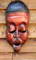 Front view of hand carved wooden African mask with closed eyes and stylized facial features, mounted on wooden background.