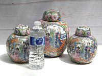Photo of three Famille Rose ginger jars in front of a white backdrop with a water bottle for scale.