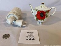 Two ceramic night lights laid flat; one shaped like a teapot with red flower design, other a cylindrical cream light.