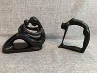 Two small black ebonized wood abstract sculptures side by side on a neutral fabric background, showing size and relative shapes.