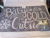 Photo of the full outdoor mat showing the design and text 'Baby it's COLD Outside' with snowflakes.