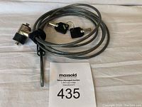 Full view of coiled silver cable lock with attached lock mechanism and two keys lying on a white surface.