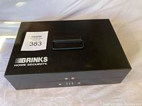 Top view of black rectangular metal cash box showing handle and Brinks Home Security logo