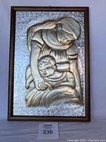 Front view of framed embossed metal art showing a mother holding a child, well lit with slight shadowing