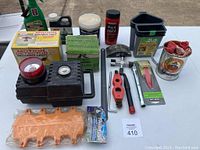 Top view of lot showing portable compressor with pressure gauge and light, terminal cleaner set, generator light set boxes, small hand tools, and other garage items.