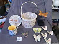 Lot of butterfly-themed items including ceramic plate, basket, mug, and various butterfly figurines and ornaments shown on table.