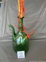 Full view of tall green glass wine bottle with spout and stopper adorned with orange string against a grey backdrop.