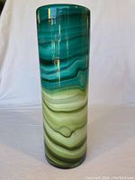 Front view of a tall cylindrical art glass vase with a swirl pattern in green, teal, and cream colors, showing glossy finish and color gradient details.