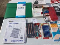 Photo showing various office supplies including d:vice envelope sleeve, DG Office index dividers, Pentel pens, pencils, and other small organizing items.
