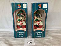 Two large blue boxes each containing a Christmas Mickey Mouse glass ornament. Both boxes show the Mickey Mouse logo and price tags.