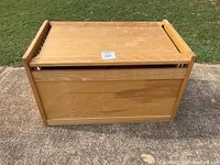Front view of large wooden toy box on outdoor pavement with hinged lid closed.
